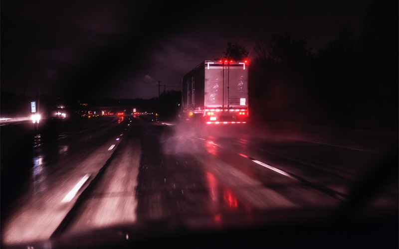A semi-truck drives over a rain-slicked road at night.