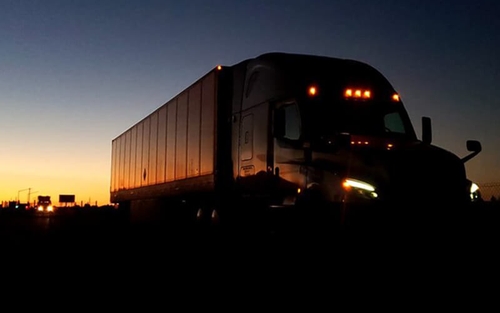 A Schneider semi-truck hauling a trailer with a sunset behind it.