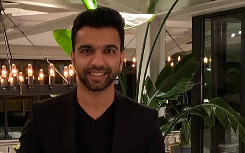 Schneider associate Akshay Patil is nicely dressed in a modern-style room decorated with contemporary light fixtures and tropical plants.