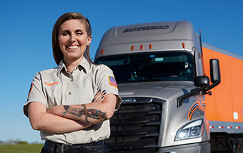 KayLeigh McCall stands in front of her Schneider truck and trailer with her tan training engineer shirt on.