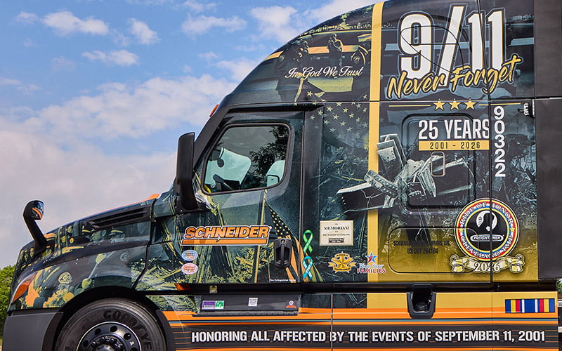 The driver side of Schneider's 2026 Ride of Pride truck. The truck wrap features a picture of the World Trade Center cross; a structural steel beam found in the rubble of the site shortly after the collapse.