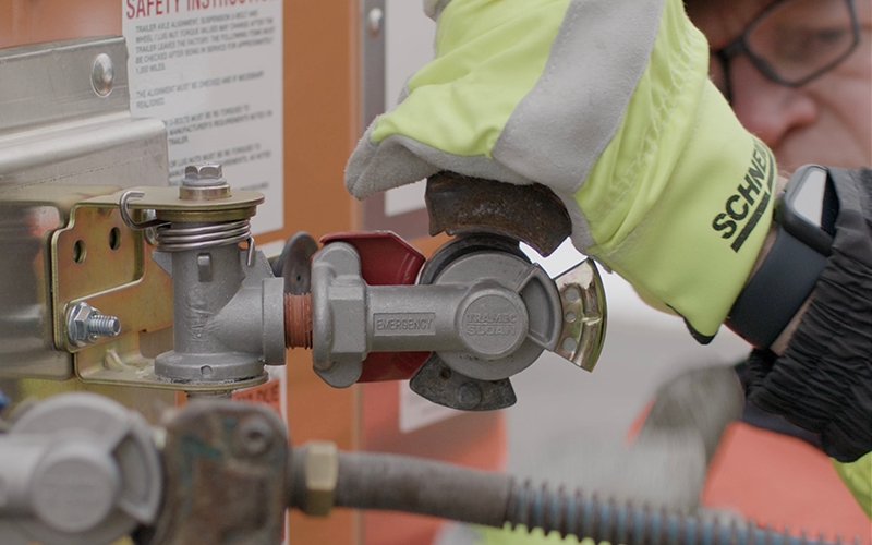 A truck driver wearing hi-vis canvas gloves connecting an air line between their tractor and trailer. 