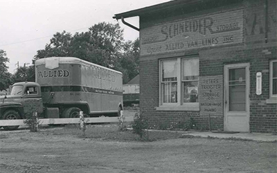 A vintage Schneider truck parked outside a company office in the 1950s
