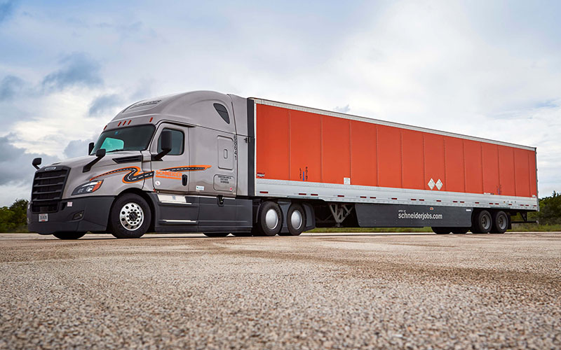 A Schneider semi-truck parked in a lot with a cloudy sky in the background.