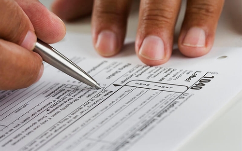 Someone is filling out a paper 1040 tax form with a silver pen.