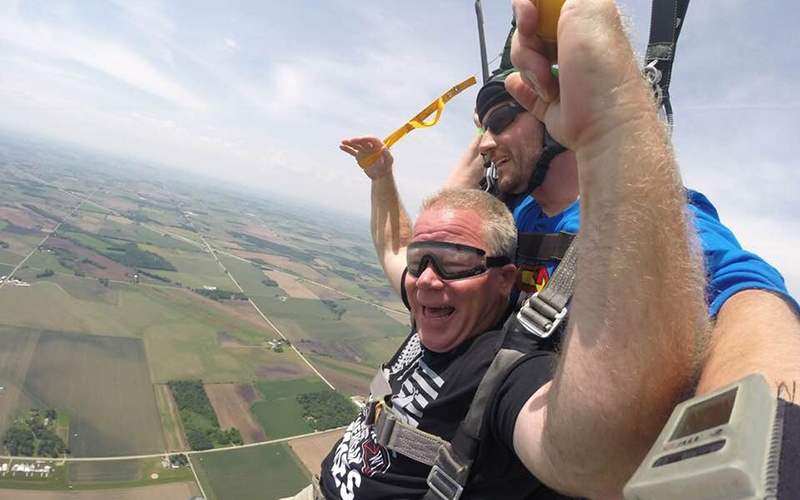 Schneider driver and veteran Chip Hill smiles widely while gliding back to the ground with his skydiving instructor.
