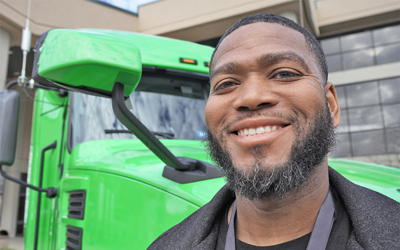 A man standing in front of a green semi-truck cab.
