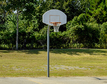 A basketball hoop with a white backboard and orange hoop sits unused at a public basketball court.