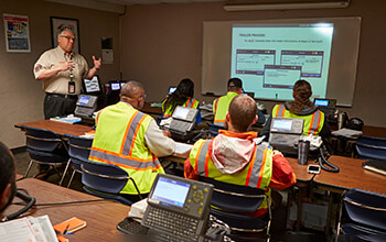 A truck driver instructor teaches new drivers in a classroom.