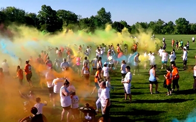 Volunteers release colored powders into the air for runners at color run event.
