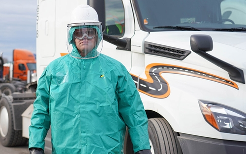 A HazMat driver in their PPE standing outside of their tractor-trailer.