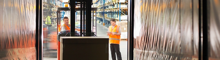 A Schneider associate drives a forklift into the back of an open trailer while another observes holding a clipboard