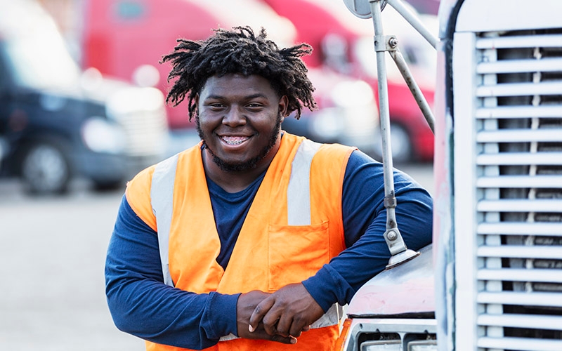 A man wearing a safety vest stands in a parking lot.