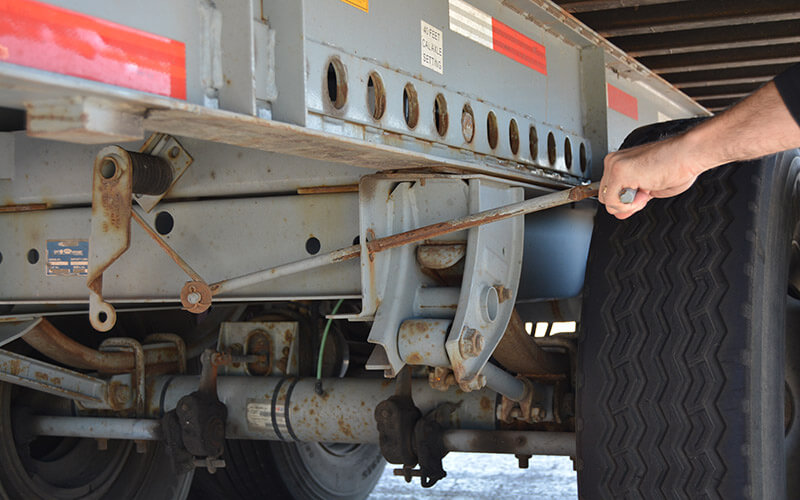A driver's hand pulls on a handle near the rear wheels of an Intermodal container to engage the spring on the EZ Pull tandem release system of the trailer.
