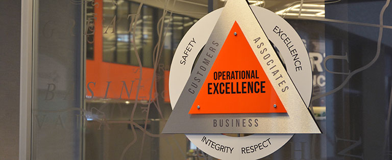 An operational excellence emblem is displayed on a glass divider outside a vast office area at Schneider's corporate headquarters