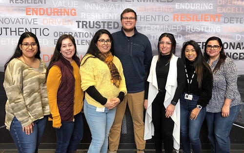 Schneider's Bilingual Driver Recruiting Team stands in a line in front of a Schneider-branded wall.