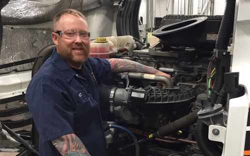 A Schneider diesel technician smiles for the camera while working on a company truck