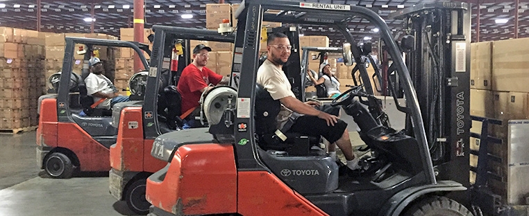 Four Schneider warehouse associates each sit in forklifts with pallets behind them