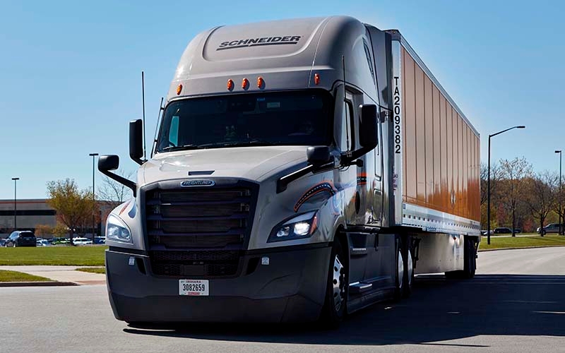 A Schneider semi-truck with a grey tractor driving on an empty road.