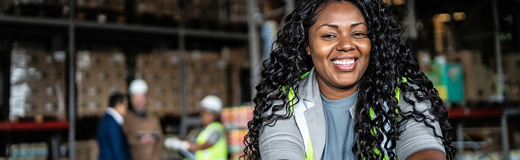 A Schneider warehouse associate poses in front of pallets loaded with packages with three associates in the background