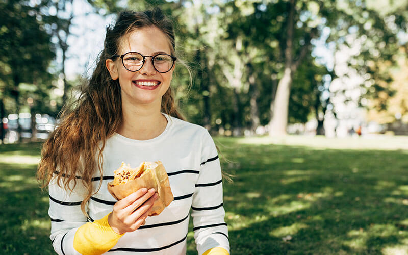An associate sits in a grassy area of a public park, eating a packed lunch.