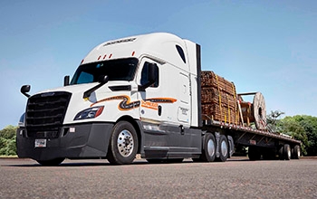 A white semi-truck hauling a flatbed trailer with wood is parked at an angle in a parking lot.