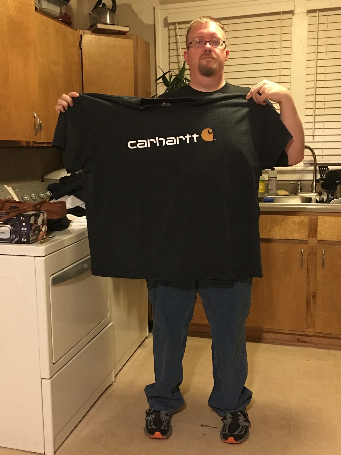 Aaron holds an old Carhartt t-shirt up to his body to show the extent of his weight loss.