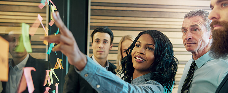 A Schneider supply chain associate gestures at information on sticky notes while her colleagues observe and listen nearby