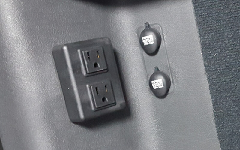 A black plastic outlet is next to two power inverters in a semi-truck interior.