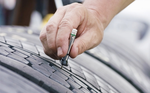 A close-up view of a hand using a tire tread depth gauge to measure the tread depth on a semi-truck tire.