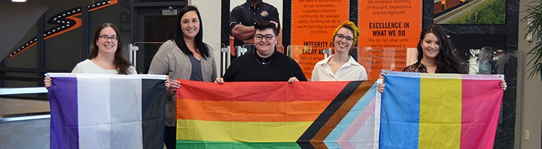 Members of Schneider's LGBTQIA+ business resource group stand holding three different pride flags.