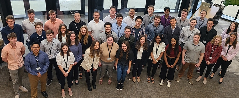 A group of seven Schneider interns pose together in the lobby area of the corporate headquarters.