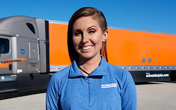 Kayleigh McCall smiles and stands in front of a grey Schneider tractor hauling an orange trailer.