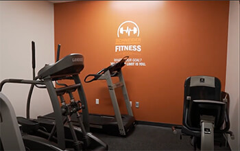 A Schneider fitness facility with a bright orange wall has fitness equipment like an elliptical, treadmill and stationary bicycle.