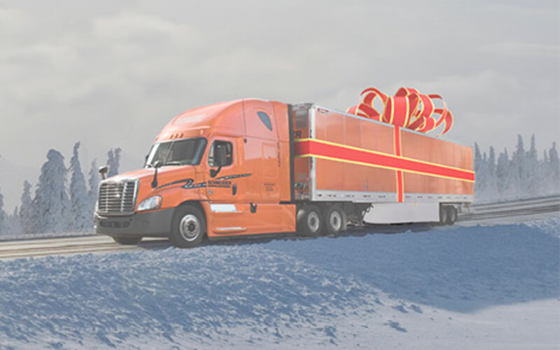A Schnieder truck hauls an orange trailer that's wrapped with a present ribbon 