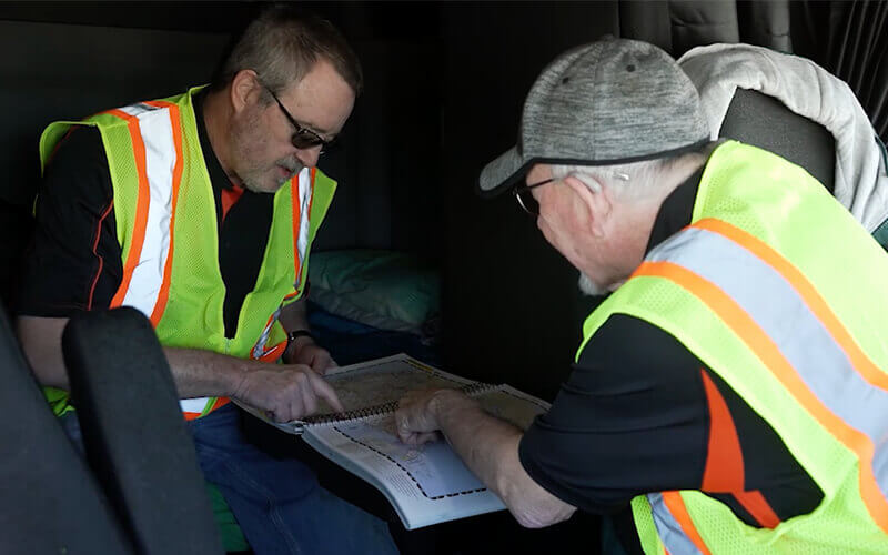 Two Schneider truck drivers do some trip planning in the cab of their truck.