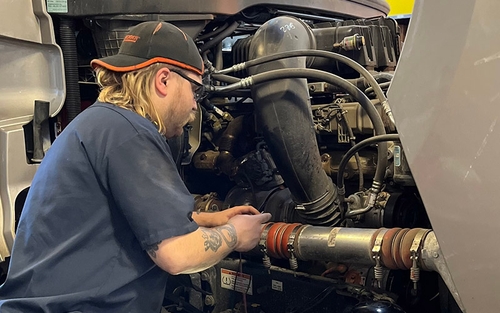A man works on a semi-truck's diesel engine.