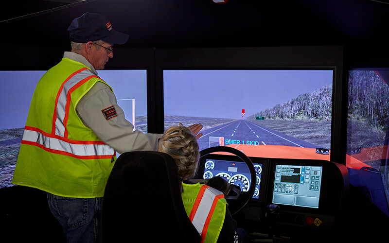 Truck driver trainer shows a driving student how to work a driver simulator.