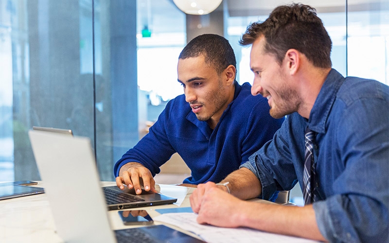 Two men sitting at a table and looking at a computer screen.