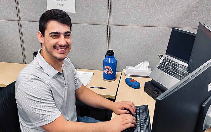 A young man sits at his desk with his hands on his keyboard.