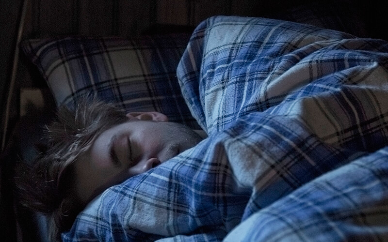 A man sleeps in a bed with blue flannel sheets on it.