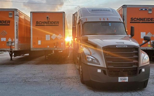 A Schneider tractor backs up to an orange Schneider trailer, with other trailers surrounding it.