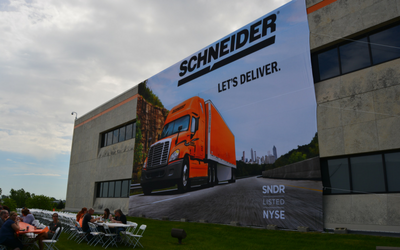 A two-story banner draped over the side of the corporate office building depicts a Schneider semi-truck with words "Let's deliver."