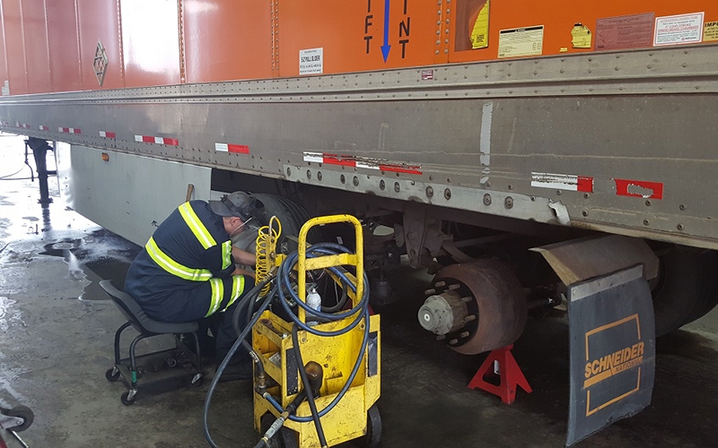 A Schneider trailer technician works on the wheels of a company trailer.