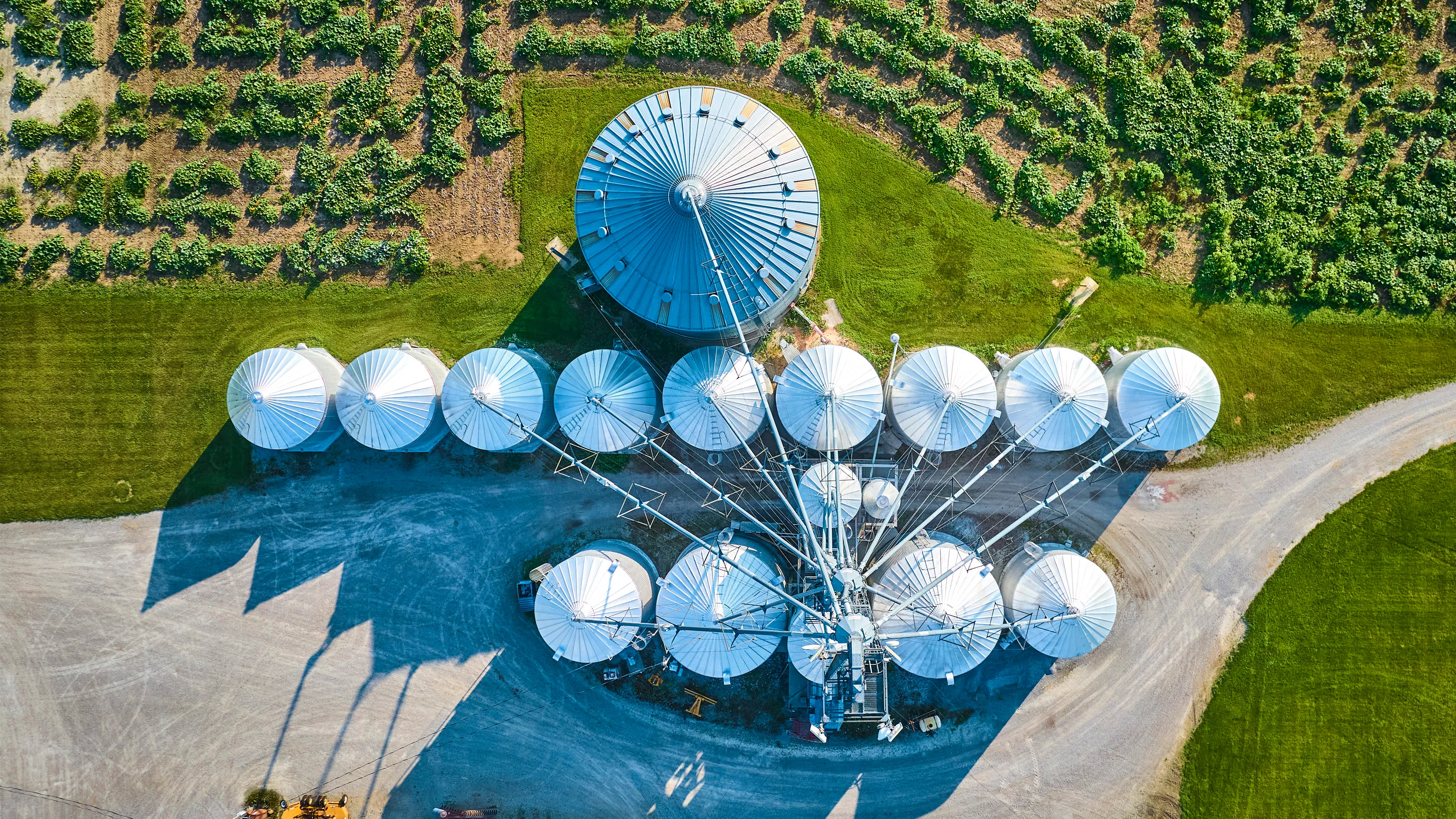 Aerial view of a large agricultural grain facility with multiple circular storage silos, access roads and surrounding farmland