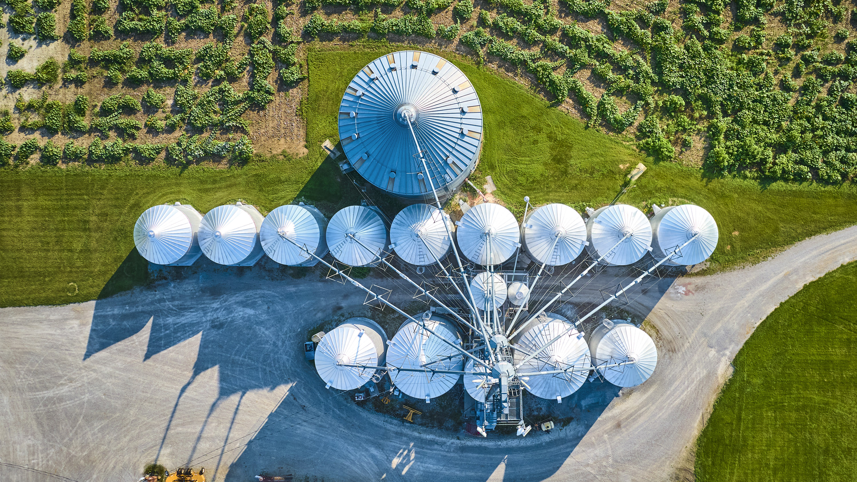 Aerial view of a large agricultural grain facility with multiple circular storage silos, access roads and surrounding farmland