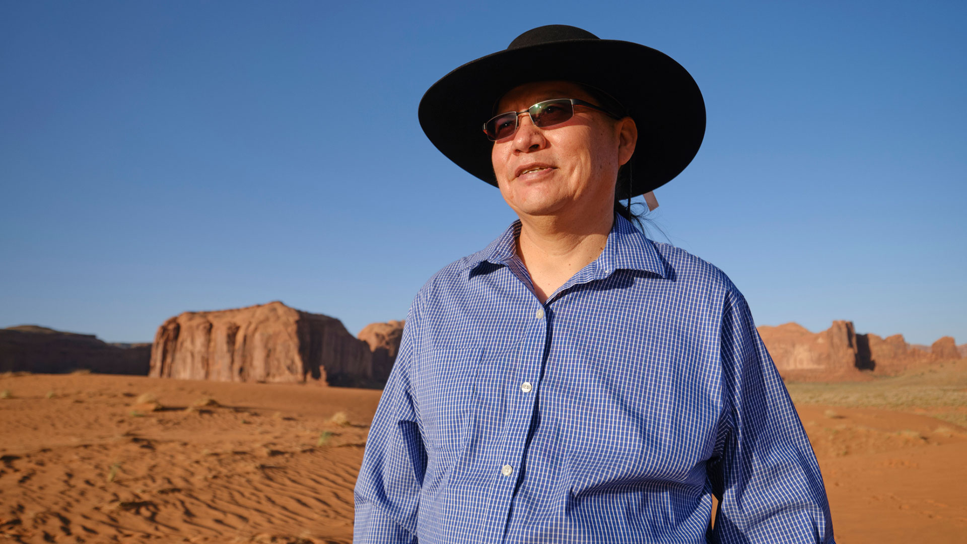 Native American wearing hat and sunglasses standing in desert