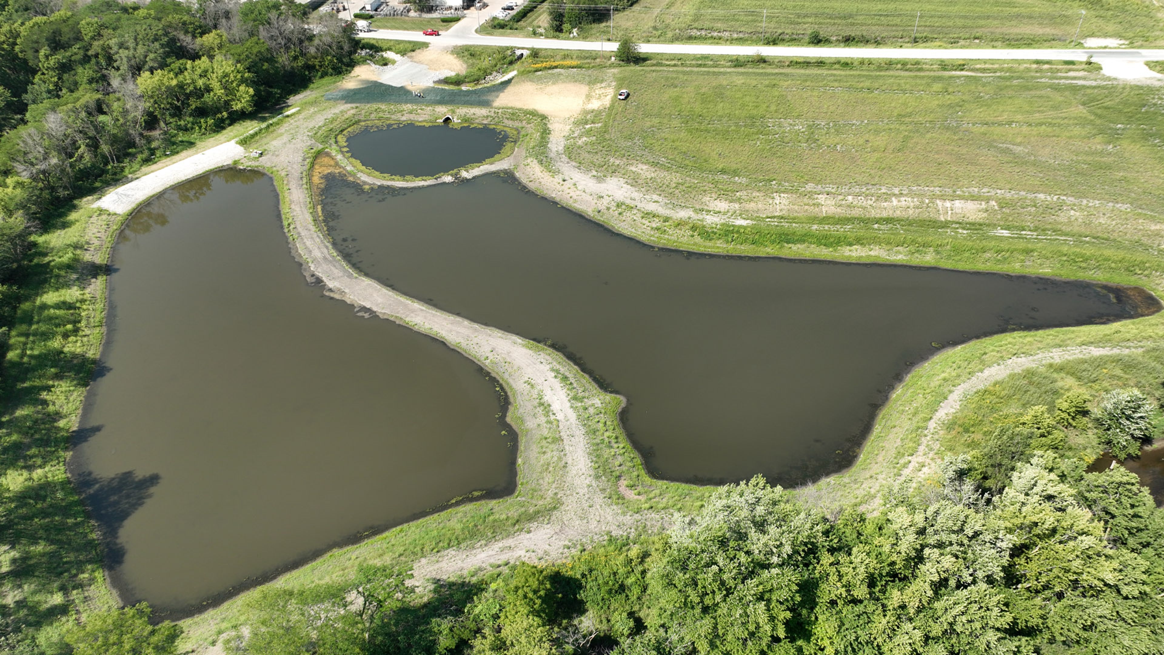 A drone view of several connected water ponds surrounded by grassy fields and trees.