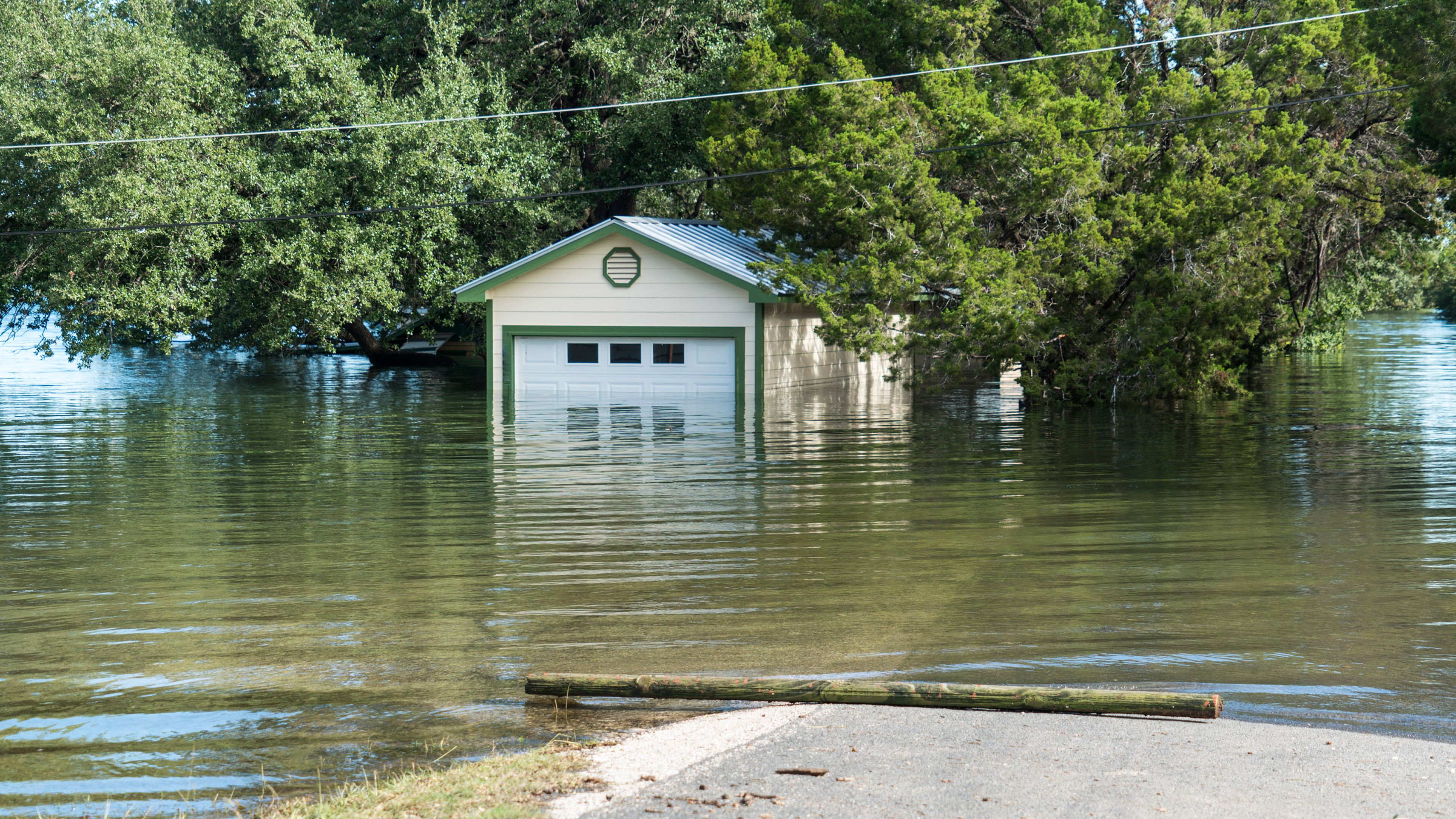 A small building partially surrounded by floodwater with trees and muddy water covering the surrounding area