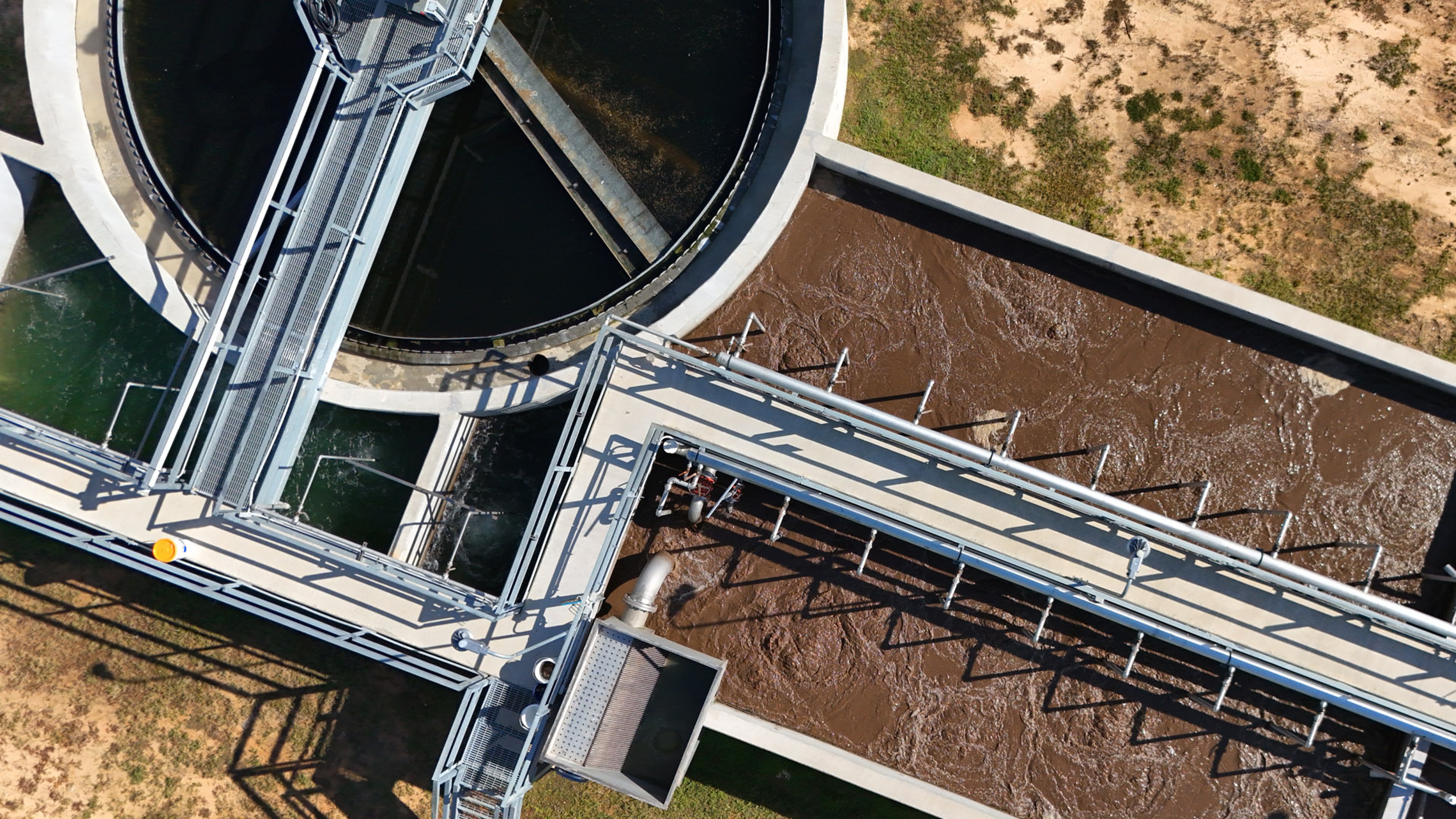 Aerial view of a water treatment facility with circular and rectangular processing tanks.